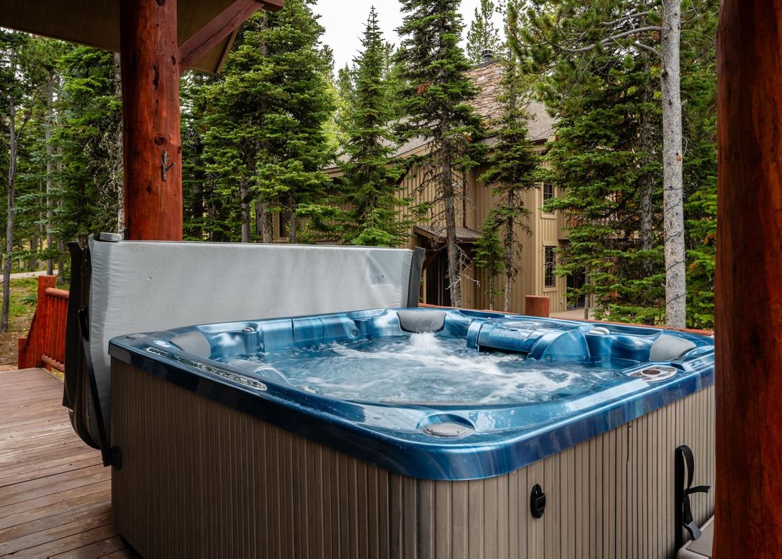 The bubbling hot tub on the wooden deck of Moonlight Mountain 38B Cowboy Heaven, surrounded by lush pine trees.