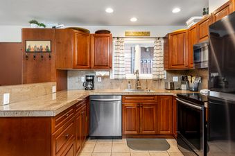 A fully equipped kitchen at All Seasons 2 Bedroom Platinum Unit A1B features wooden cabinets, granite countertops, and modern stainless steel appliances including a dishwasher, microwave, and refrigerator.