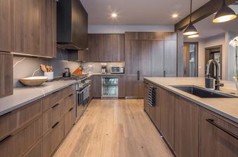 A modern kitchen in Headwaters Hideout with rich wood cabinetry, grey quartz countertops, a large island with a sink, and stainless steel appliances.