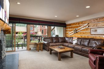The comfortable living room at Montaneros 216 features a brown leather sectional, a rustic coffee table, a stone fireplace, and a flat-screen TV.