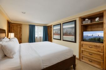 A cozy bedroom in Montaneros 417 features a large bed with white linens, a TV, and charming decor.