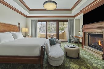 A luxurious bedroom at the Montage Two Bedroom Empire Suite featuring a large wooden bed, a sitting area, a fireplace, and a private balcony overlooking a snowy landscape.