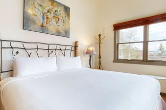 A king-sized bed with white linens and a decorative metal headboard in a bedroom with a large window and a world map artwork on the wall.