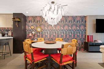 A vibrant dining area with a round table and six chairs with red cushions, under a unique chandelier, transitioning into a modern kitchen area in The Charter L022.
