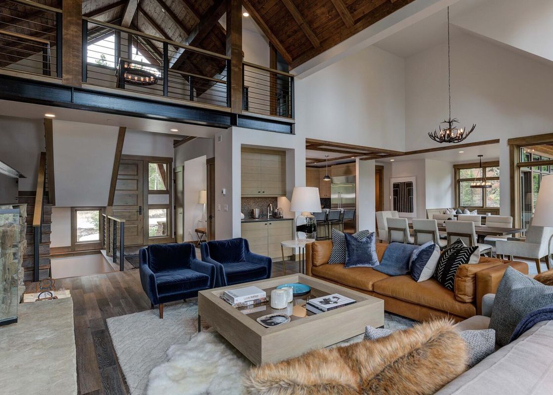 Moonlight Basin 6 Diversion Lane living room with large windows looking out at the mountains, leather couch with pillows and throw blankets, a coffee table in front of the couch, and two chairs.