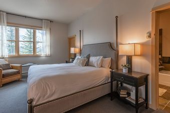 A master bedroom with a king-size bed, armchair by the window, and an en-suite bathroom in Moose Creek 1.