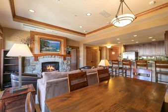A large living room with a stone fireplace, a large flat screen TV, and a dining table in the foreground.