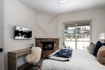 The master bedroom at Moonlight Basin 9 Wildwood features a fireplace, a large window with views of the snowy mountains and a cozy bed.