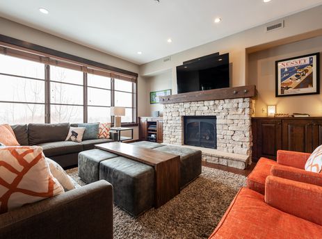 A cozy living room at Silver Star 1304 with a stone fireplace, sectional sofa, and orange armchairs.