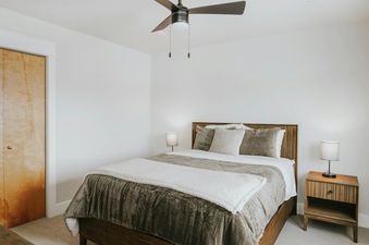 A cozy bedroom in The Circle Unit B features a comfortable bed with neutral-toned bedding, two nightstands with lamps, and a closed wooden closet.