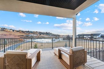 A private balcony at Deer Valley Modern with two outdoor chairs offers panoramic views of rolling hills, distant townhouses, and a bright, cloudy sky.