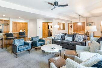 A spacious and elegantly furnished living area in Christie Club 306 features a large sofa, multiple armchairs, a coffee table, and an adjacent kitchen bar, all under soft lighting.