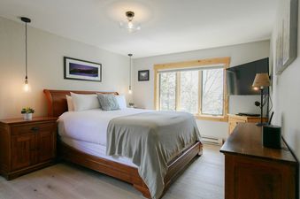Cozy bedroom at Teewinot B4 with wood bed frame, large window, and wall-mounted television.