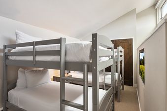 A bunk room at Vail 21 407 featuring two grey bunk beds with white linens, a high window, a small framed landscape image in a wall recess, and a wooden door.