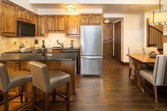 Fully equipped kitchen with wooden cabinetry, stainless steel appliances, breakfast bar, and adjoining dining table.