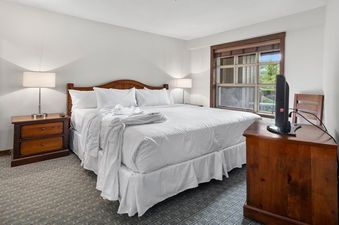 The bedroom at Blackcomb Springs Two Bedroom Slopeside Suite features a king-sized bed, two nightstands with lamps, a dresser, and a TV.