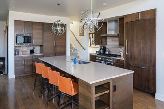 The modern kitchen at Moonlight Basin 6 Silver Peaks has stainless steel appliances, dark wood cabinets, a large island with bar stools, and a view of the stairs leading up to the upper level.