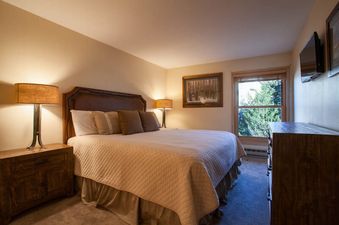 A cozy bedroom at Kutuk 203 with a king-sized bed, rustic wood furniture, and a window showing green trees.