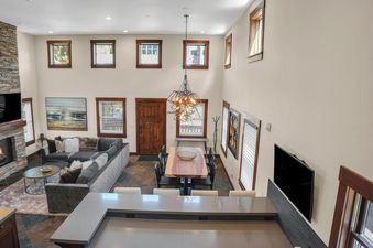 An elevated view of the great room at The Peak at Town Lift, showcasing a living area with a stone fireplace and a dining space with a wooden table under a geometric chandelier.