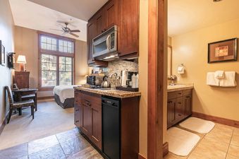 A hotel room with a kitchenette, a bedroom, and a bathroom.