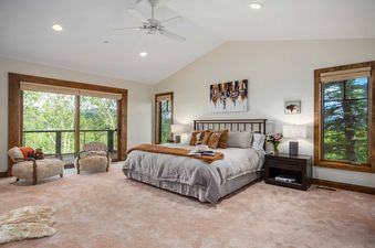 A master bedroom with a king-size bed, wood-framed windows, and armchairs in a luxurious mountain retreat.