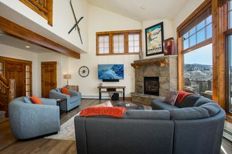 The living area of EagleRidge Townhomes 1461, featuring a stone fireplace, a large TV, comfortable seating, and mountain views from the windows.