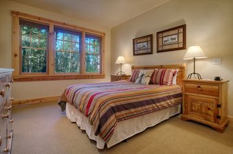 A cozy bedroom at Granite Ridge Homestead 3072 featuring a striped comforter and wood furniture with a view of the forest.