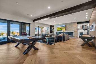 A games room with a billiard table, a living area with a large TV, and expansive windows showcasing mountain views with autumn trees.