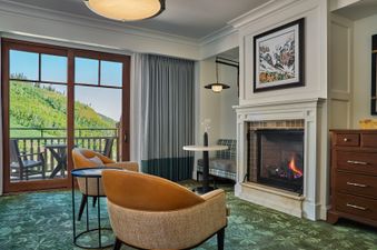 A luxurious resort room at Montage Deer Valley with a lit fireplace, comfortable seating, and a balcony overlooking lush green mountains.