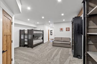 A cozy bunk bedroom at Alpine Glow Ski Haus features a dark wooden bunk bed, a comfortable sofa, and ski-themed decor, with a warm wooden door to the left.