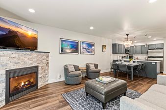 A modern and cozy living area at Snow Flower 137 with a stone fireplace, plush seating, and an adjacent dining area and kitchen.