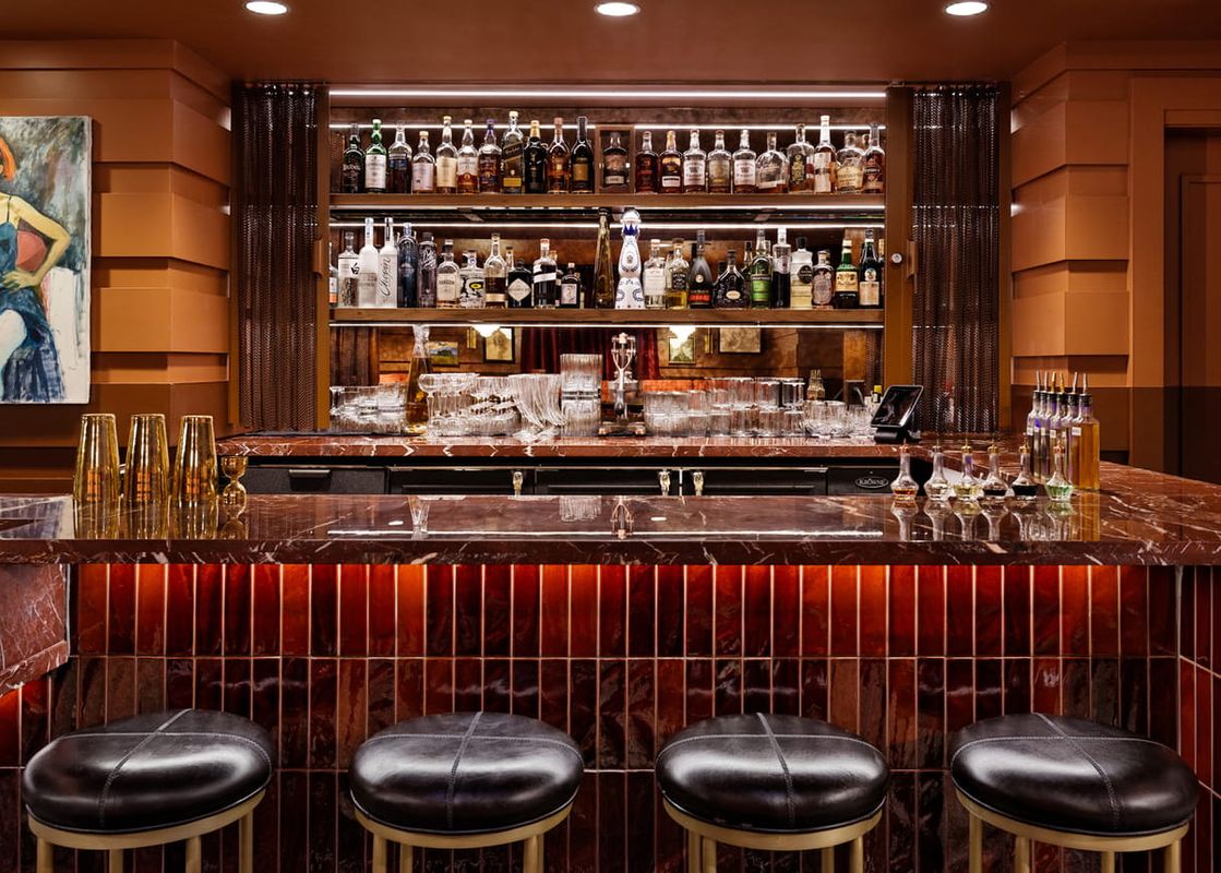 A sophisticated bar area within the Four Seasons Mountain Side Room, featuring a dark marble countertop, leather stools, and shelves stocked with various liquor bottles.