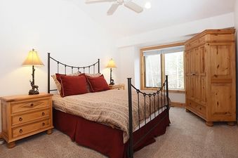 A cozy bedroom in Timberlake 341 features a large bed with a black wrought iron frame, two matching nightstands with elegant lamps, and a wooden armoire, all set against white walls.