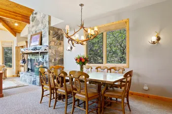 A dining table with six chairs set in the dining room of Trails End Lodge 18, with a fireplace in the background.