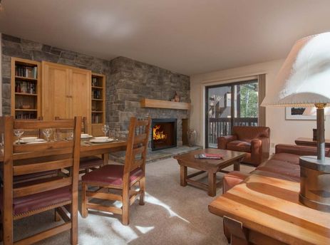 A cozy living room with a fireplace, a large leather couch, and a wooden dining table set.