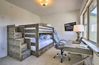 A bunk room at Rendezvous Retreat features a wooden bunk bed with stairs leading to the top bunk, a desk with a laptop and lamp, and a wall-mounted TV.
