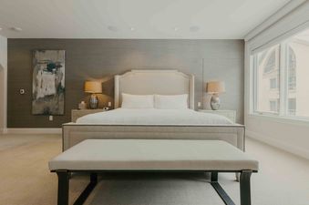 A spacious master bedroom at Sanctuary Chalet at One Beaver Creek, featuring a large bed with a beige upholstered headboard, white bedding, and two bedside tables with lamps.