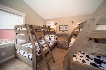 A cozy bedroom with two wooden bunk beds featuring cow print bedding and a wooden dresser in between, offering ample sleeping space.