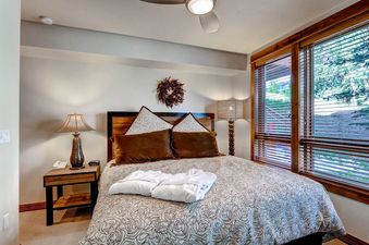 A cozy bedroom in BlueSky Breckenridge 204 with a patterned bedspread, warm lighting, and a window with blinds.