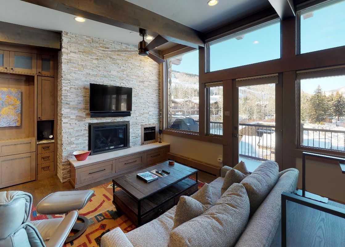 A living room with a fireplace, large windows, and a couch facing a mountain view.
