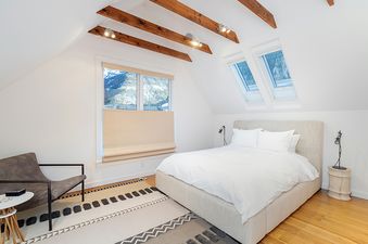 A bedroom with a bed, a chair, a rug, a window, and a skylight.