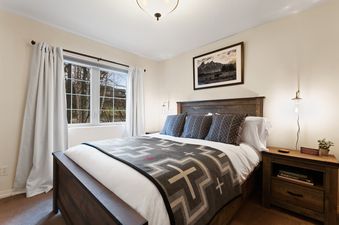 A cozy bedroom with a large wooden bed, patterned blanket, and a window offering an outdoor view at Meadow Lake Villa.