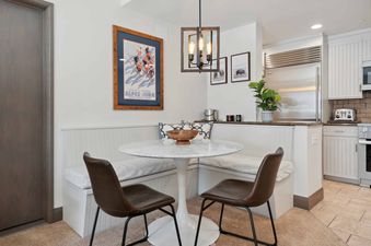 The dining area in The Charter F2305 features a round marble table, built-in bench seating, and two brown leather chairs, with a vintage ski poster and bison prints adorning the walls.