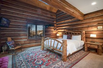 A rustic bedroom in Moose Drool Lodge featuring log walls, a wooden log bed, and a colourful patterned rug.