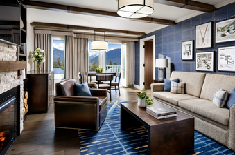 A luxurious and spacious living room, featuring a fireplace, a comfortable sofa and armchair, and a dining area, with a stunning mountain view visible through large windows.