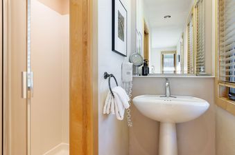 A bright bathroom in Tamarack 01 featuring a pedestal sink, a wall-mounted hair dryer, and a shower with a glass enclosure.