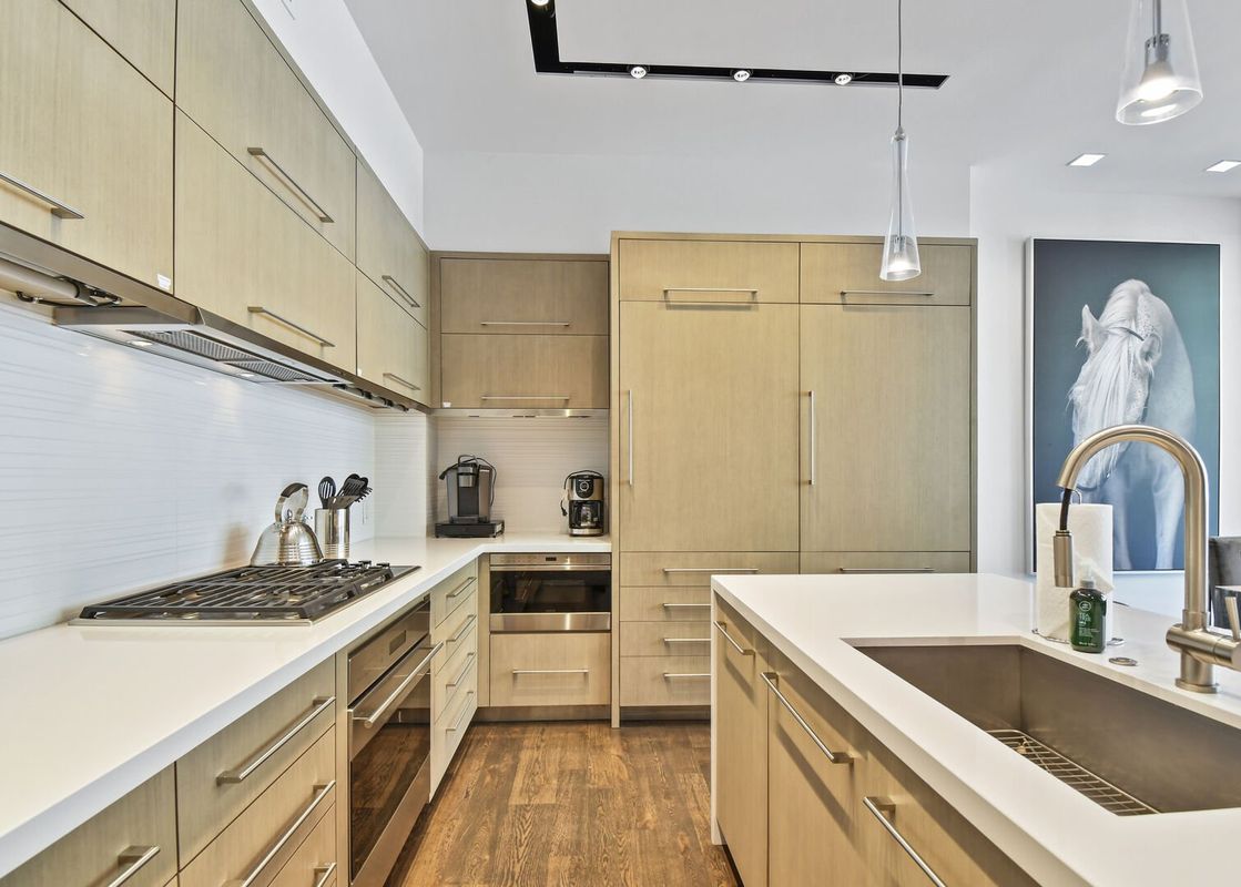A modern kitchen with light wood cabinets, white countertops, and stainless steel appliances.