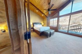 A bedroom with a king-sized bed, wood floor, and large windows with mountain views