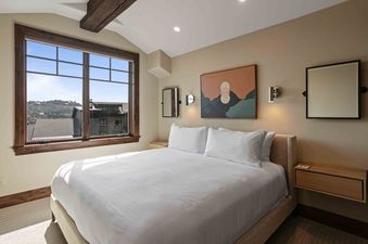 A luxurious bedroom at Silver Strike Lodge 706 featuring a king-sized bed with white linens, wooden nightstands, modern wall art, and a large window offering scenic mountain views.