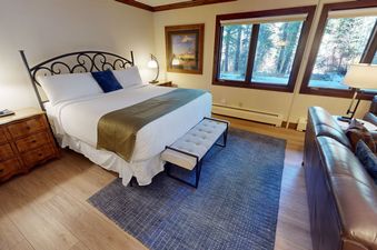 A hotel room with a king-sized bed, a dresser, and a couch with a view of trees outside of the window.